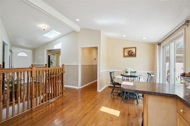dining room with baseboards, light wood-style flooring, a wainscoted wall, and vaulted ceiling with skylight