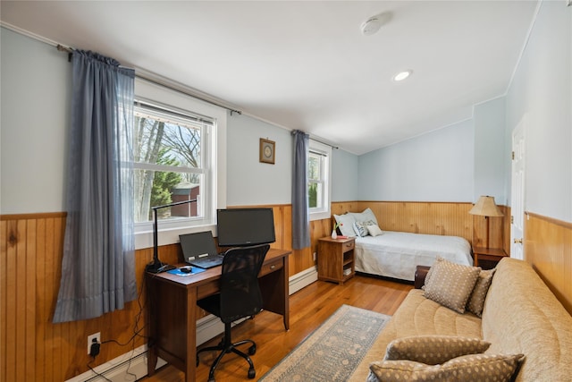 bedroom with baseboard heating, wood finished floors, a wainscoted wall, a baseboard heating unit, and wooden walls