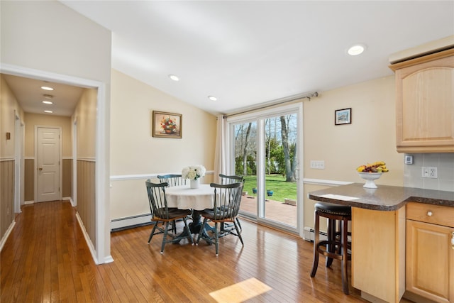 dining space with vaulted ceiling, baseboard heating, wainscoting, and wood-type flooring