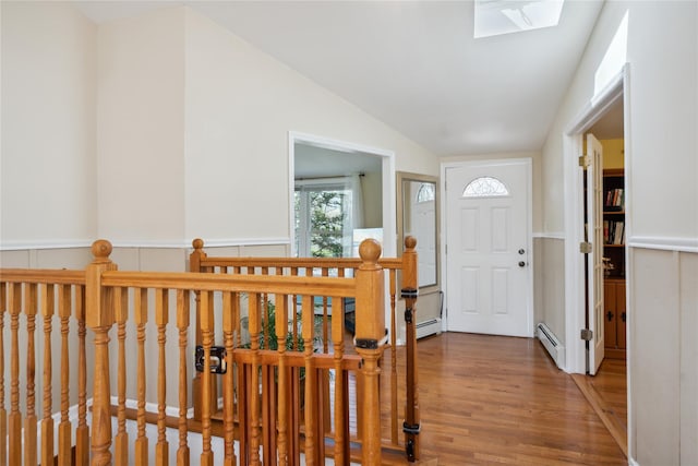 entrance foyer with a baseboard radiator, lofted ceiling with skylight, and wood finished floors