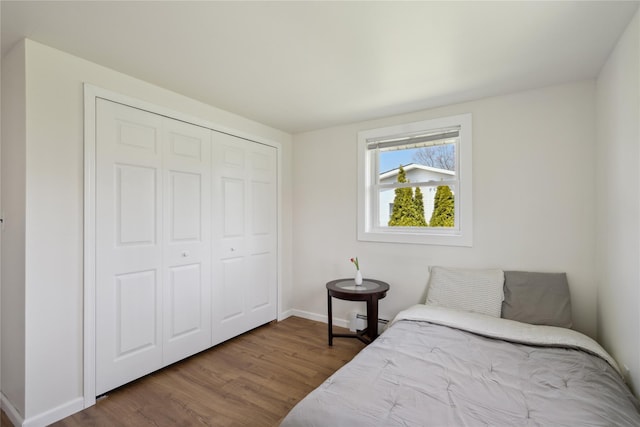 bedroom with a closet, a baseboard heating unit, baseboards, and wood finished floors