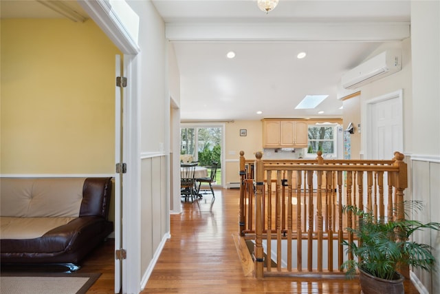 interior space with a skylight, baseboard heating, an AC wall unit, an upstairs landing, and light wood-style flooring