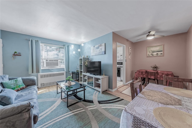 living area with radiator heating unit, cooling unit, light wood-type flooring, and ceiling fan