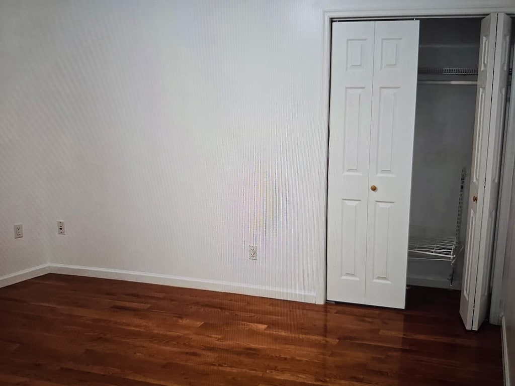 8712 175th St Unit 6A, Jamaica, NY 11432 - unfurnished bedroom with baseboards, a closet, and dark wood-style flooring
