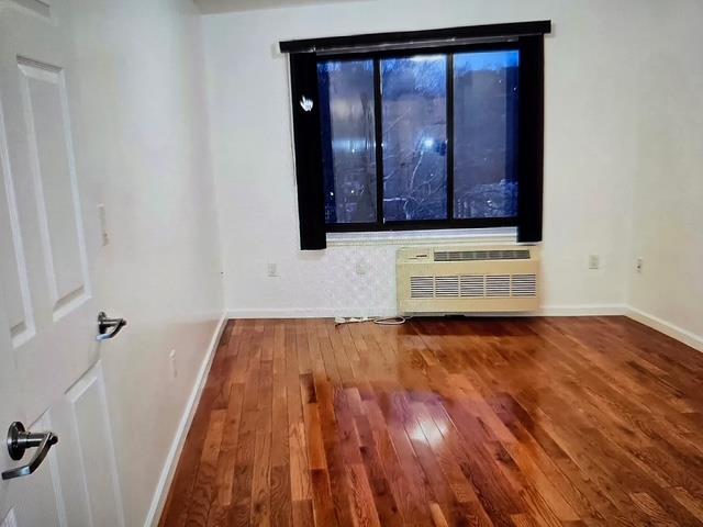 8712 175th St Unit 6A, Jamaica, NY 11432 - spare room with a wall mounted AC, hardwood / wood-style floors, and baseboards