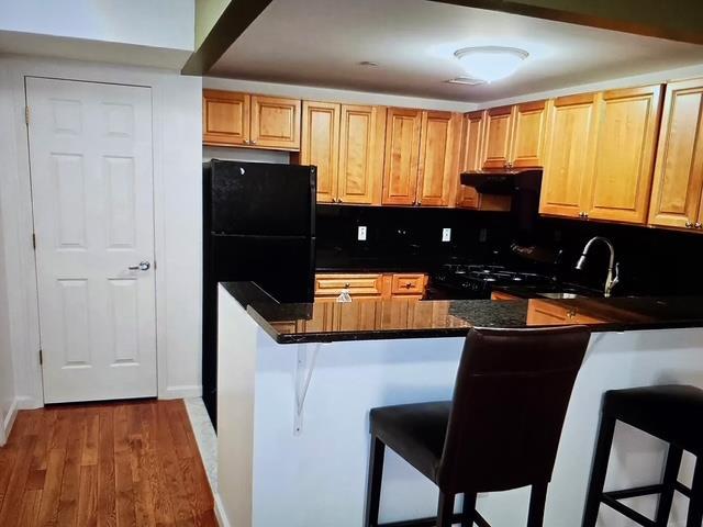 8712 175th St Unit 6A, Jamaica, NY 11432 - kitchen featuring a breakfast bar, dark countertops, wood finished floors, a sink, and black appliances