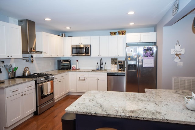 kitchen featuring stainless steel appliances, visible vents, a sink, wall chimney exhaust hood, and white cabinetry