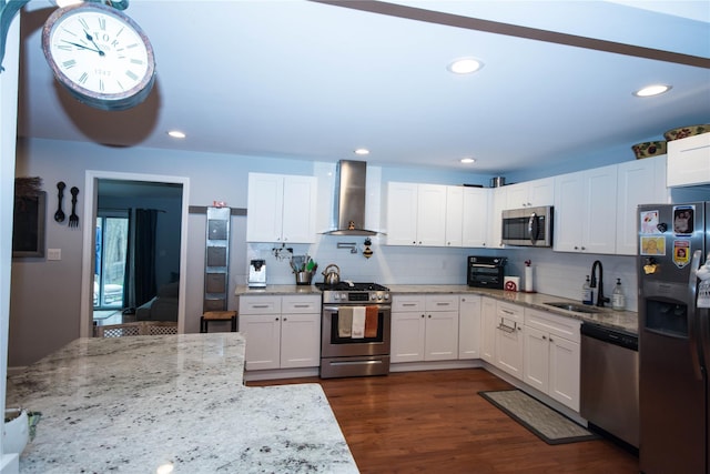 kitchen with wall chimney range hood, a sink, white cabinets, backsplash, and appliances with stainless steel finishes