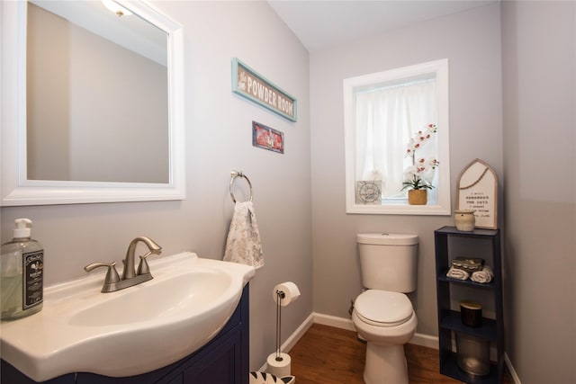 half bath featuring wood finished floors, vanity, toilet, and baseboards