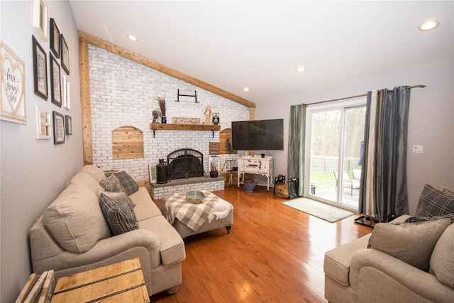 living room featuring recessed lighting, lofted ceiling, wood finished floors, a fireplace, and brick wall