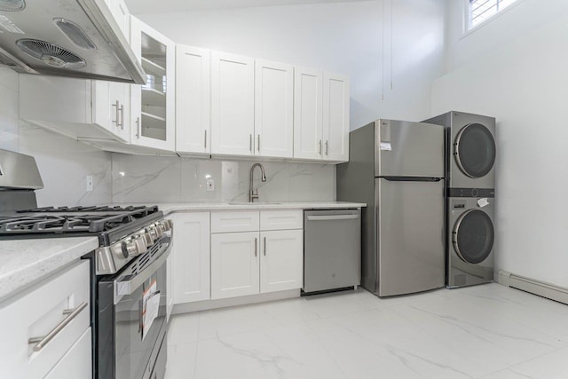 kitchen featuring a sink, stacked washer / drying machine, under cabinet range hood, stainless steel appliances, and marble finish floor