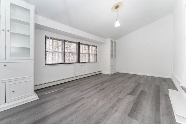 empty room with built in features, wood finished floors, vaulted ceiling, and baseboard heating