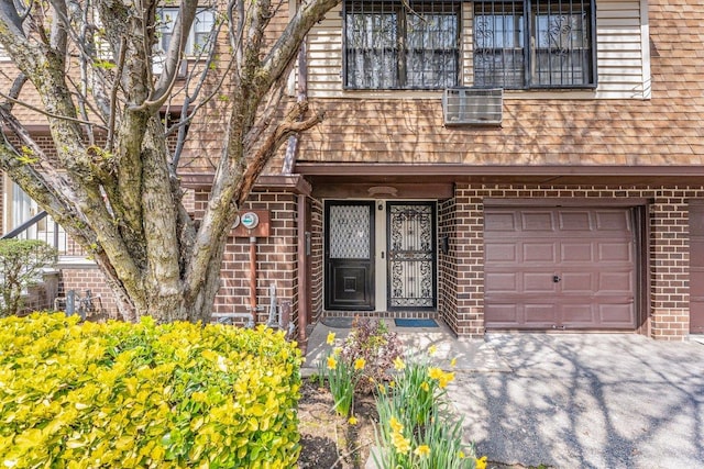 view of exterior entry featuring an attached garage, roof with shingles, driveway, and brick siding