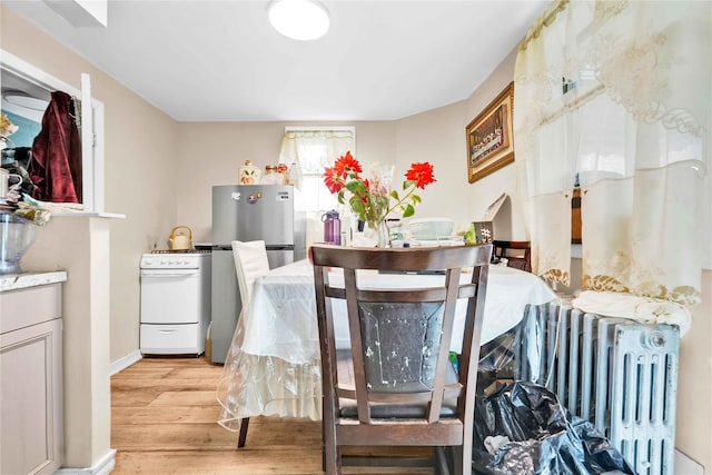 dining area with light wood-style floors, baseboards, and radiator
