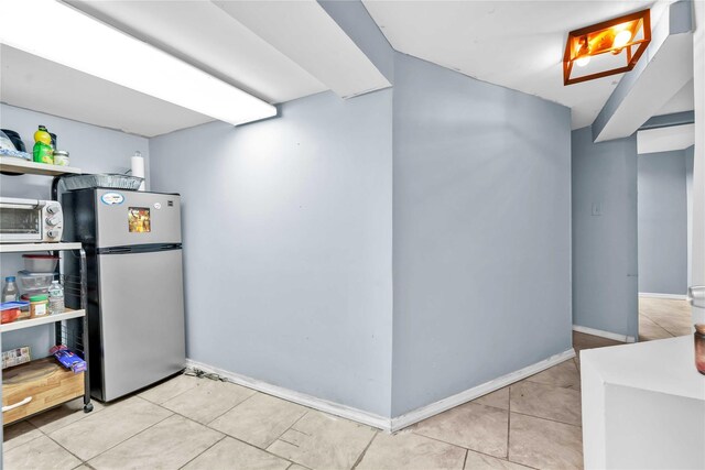 finished basement featuring tile patterned floors, freestanding refrigerator, a toaster, and baseboards