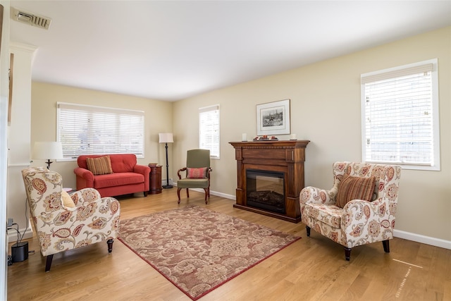 living area with visible vents, baseboards, wood finished floors, and a glass covered fireplace