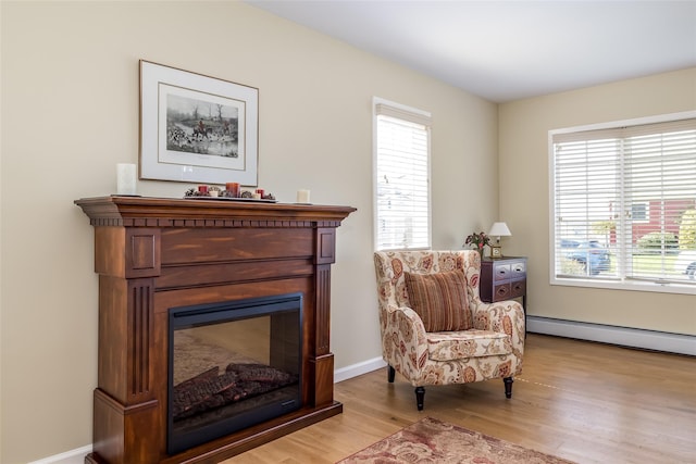 living area featuring baseboard heating, light wood-type flooring, a glass covered fireplace, and plenty of natural light