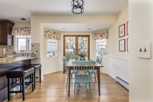 dining room with a baseboard heating unit, light wood finished floors, and baseboards