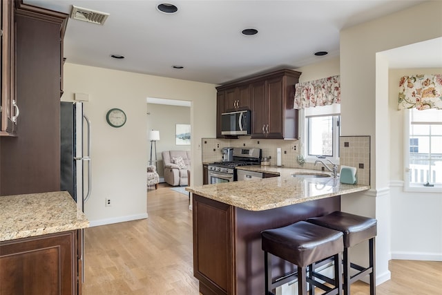kitchen featuring appliances with stainless steel finishes, dark brown cabinetry, light stone countertops, and a sink