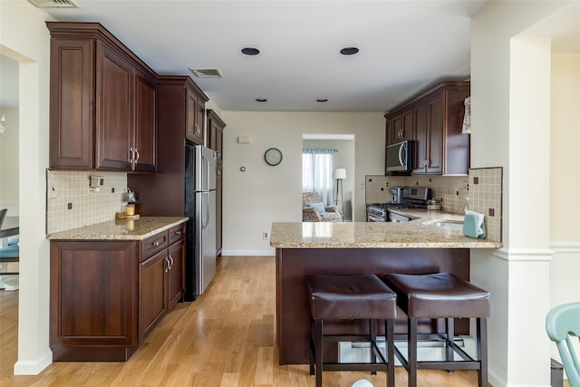 kitchen with decorative backsplash, a breakfast bar, appliances with stainless steel finishes, light wood-type flooring, and visible vents