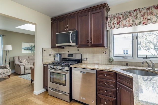 kitchen featuring light stone countertops, light wood-style flooring, decorative backsplash, appliances with stainless steel finishes, and a sink