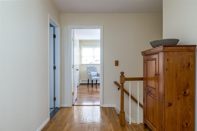 hallway featuring an upstairs landing, a baseboard radiator, light wood-style floors, and baseboards