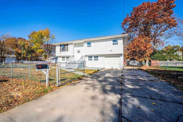 rear view of house featuring concrete driveway, a garage, and a fenced front yard