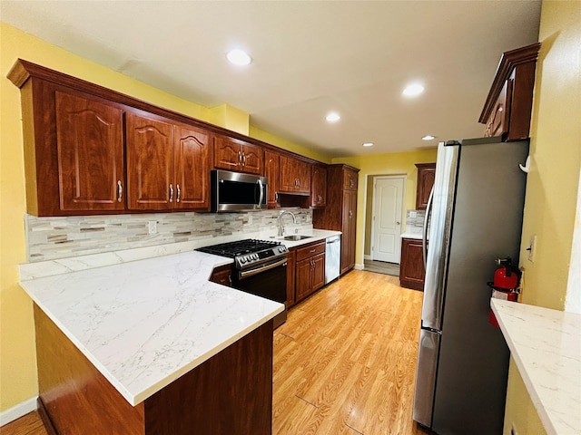 kitchen featuring a sink, backsplash, light wood-style flooring, and appliances with stainless steel finishes