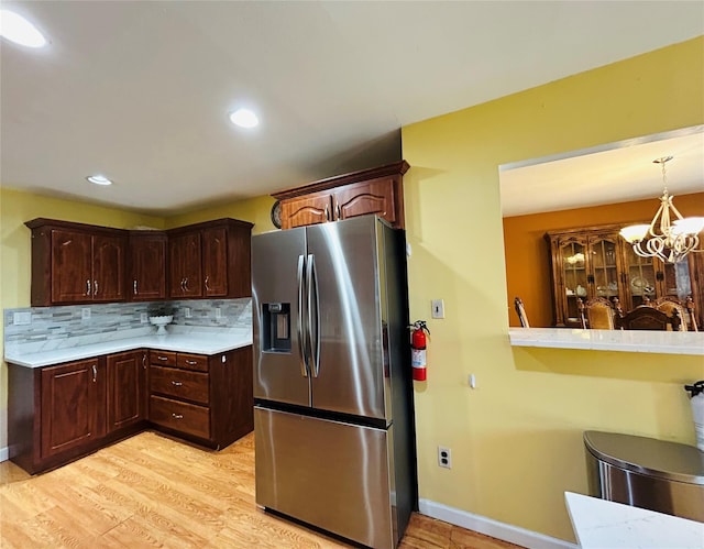 kitchen featuring baseboards, light countertops, backsplash, stainless steel refrigerator with ice dispenser, and light wood-style floors