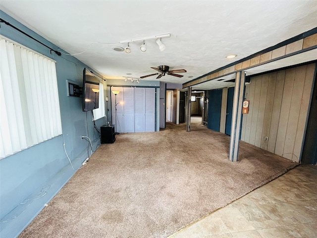 unfurnished living room featuring wood walls, a ceiling fan, and carpet