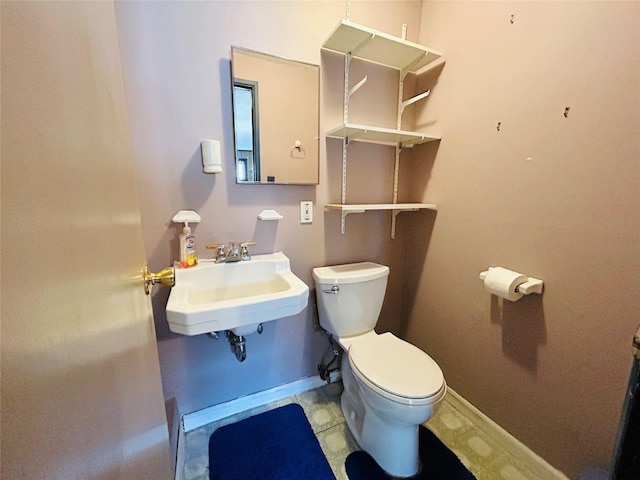half bathroom with toilet, a sink, baseboards, and tile patterned flooring