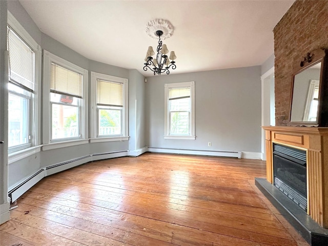 unfurnished living room featuring a glass covered fireplace, a notable chandelier, light wood-style floors, and a healthy amount of sunlight
