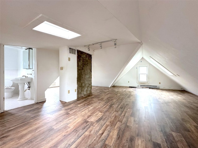 additional living space with vaulted ceiling with skylight, visible vents, a baseboard radiator, and wood finished floors