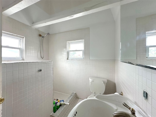 full bathroom with toilet, tiled shower, plenty of natural light, and tile walls