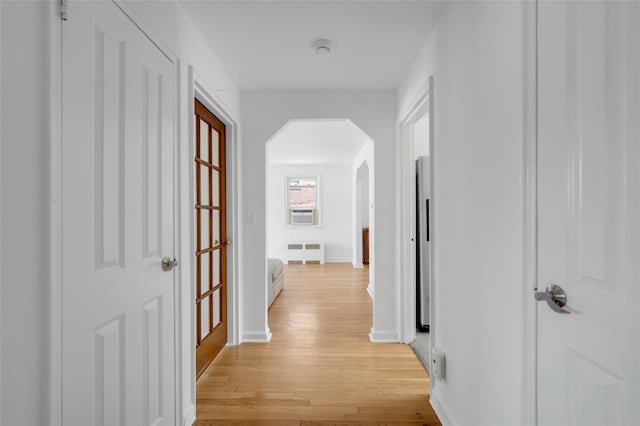 corridor with radiator, arched walkways, light wood finished floors, and baseboards