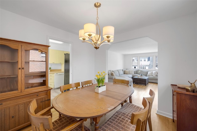 dining area with a chandelier, arched walkways, and light wood finished floors