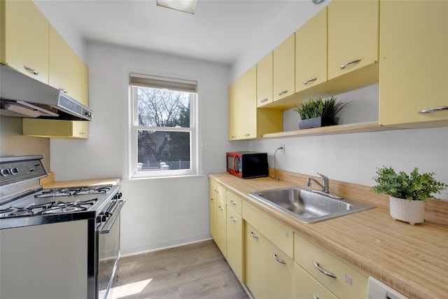 kitchen featuring stainless steel gas range oven, open shelves, light countertops, a sink, and cream cabinets