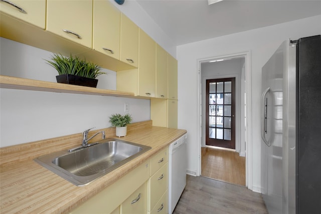 kitchen with open shelves, a sink, dishwasher, cream cabinets, and freestanding refrigerator