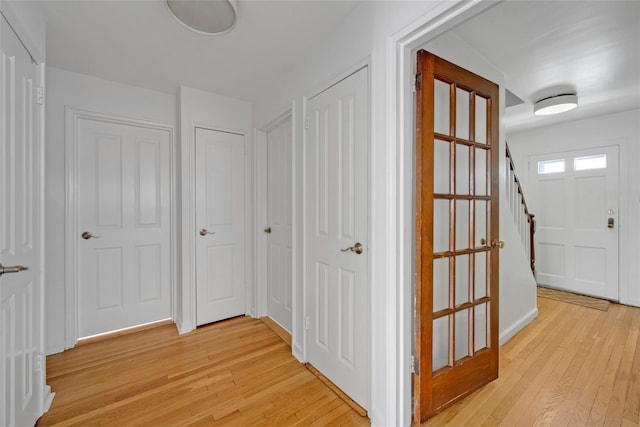 hallway with baseboards, stairs, and light wood-style flooring