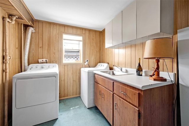 clothes washing area with a sink, cabinet space, light colored carpet, wood walls, and independent washer and dryer