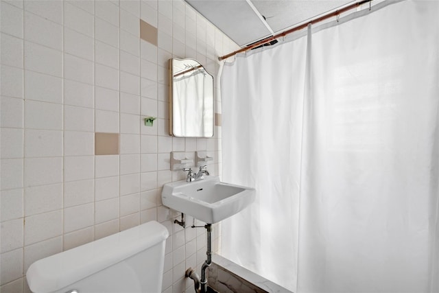 bathroom with tile walls, a sink, curtained shower, and toilet
