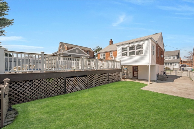 rear view of property featuring a chimney, fence, a wooden deck, a patio area, and a lawn