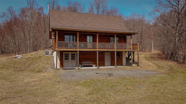 exterior space featuring a wooden deck, a view of trees, a yard, roof with shingles, and log exterior