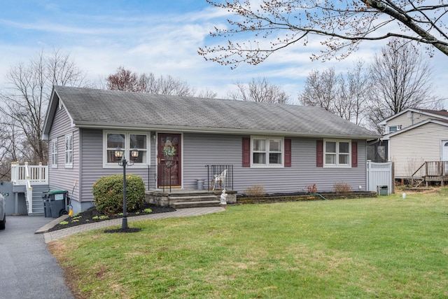 ranch-style home featuring a front lawn and roof with shingles