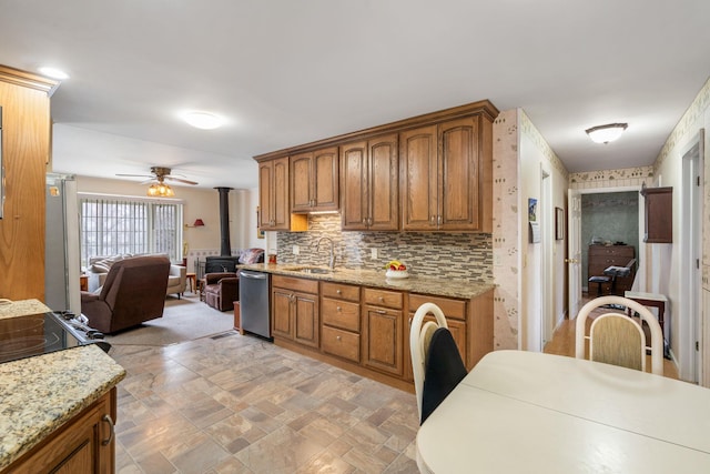 kitchen with brown cabinetry, appliances with stainless steel finishes, a sink, a wood stove, and open floor plan