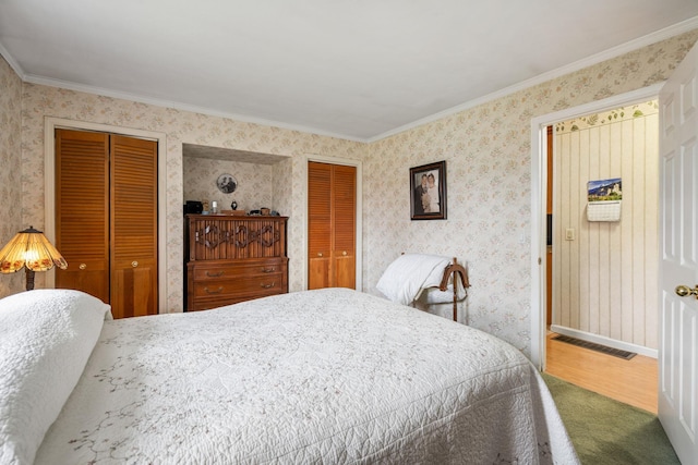 carpeted bedroom with visible vents, ornamental molding, wallpapered walls, and two closets