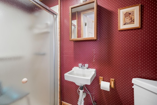 bathroom featuring toilet, a shower stall, wallpapered walls, and a sink