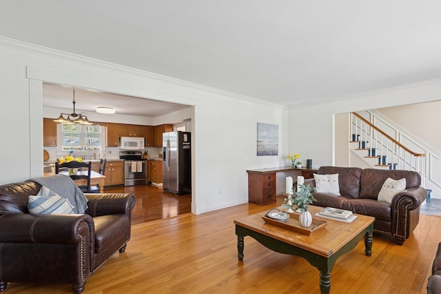 living room with stairway, crown molding, light wood finished floors, and a notable chandelier