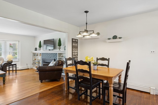dining room with an inviting chandelier, baseboard heating, a brick fireplace, a baseboard heating unit, and dark wood-style floors