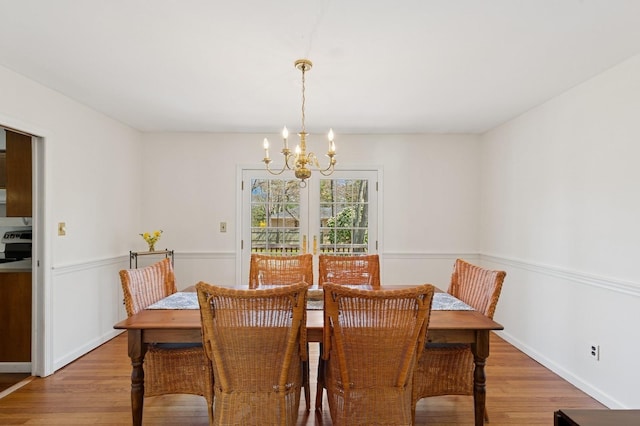 dining room with a wainscoted wall, light wood finished floors, and a chandelier